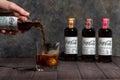 ManÃ¢â¬â¢s hand pouring Herbal Coca-Cola from bottle to ice-filled double old fashioned glass