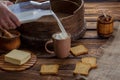 A man`s hand pours milk into a cup on the background of burlap and a wooden background. Around scattered crackers