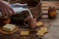 A man`s hand pours milk into a cup on the background of burlap and a wooden background. Around scattered crackers