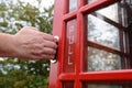 Man's hand pulls open red door of phone box Royalty Free Stock Photo