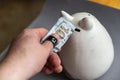 A man`s hand puts a hundred dollars in a gray piggy bank. Ceramic piggy bank in the shape of a cat. The thumb is wrapped with Royalty Free Stock Photo