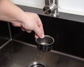 A man`s hand removes a metal strainer from a kitchen sink drain. Cleaning the drain and pipes from clogging with food particles Royalty Free Stock Photo