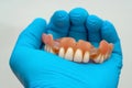 A man's hand in a rubber blue glove holds a denture.