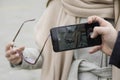 A man`s hand with a smartphone is photographing the hand of a woman in a coat holding reading glasses Royalty Free Stock Photo