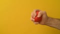 Man`s hand squeezes red anti-stress heart toy on a yellow background