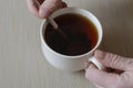 A man`s hand is stirring black tea in a mug with a metal spoon