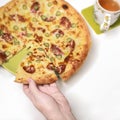 Man`s hand takes a piece of delicious Italian melted cheese pizza from a plate on a white table Royalty Free Stock Photo