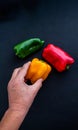 A man`s hand is taking a yellow pepper that is next to another one of different colors