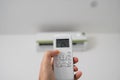 Man`s hand using remote controler. Hand holding rc and adjusting temperature of air conditioner mounted on a white wall Royalty Free Stock Photo