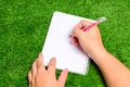 The man`s hand was holding a pen to write something down in a notebook which is on the green grass