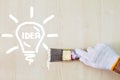 Man`s hand wearing white glove holding old grunge paintbrush and painting lightbulb on wooden wall Royalty Free Stock Photo