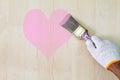 Man`s hand wearing white glove holding old grunge paintbrush and painting pink heart on wooden wall Royalty Free Stock Photo