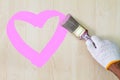 Man`s hand wearing white glove holding old grunge paintbrush and painting pink heart on wooden wall Royalty Free Stock Photo