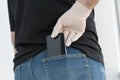 man`s hand in white medical glove takes out black smartphone from back pocket of his jeans, protection and prevention measures fr