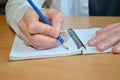 A man`s hand in a white shirt writes the text with a blue pensil in a notebook with a spiral on a wooden table Royalty Free Stock Photo