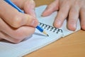 A man`s hand in a white shirt writes the text with a blue pensil in a notebook with a spiral on a wooden table