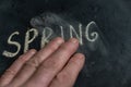 A man`s hand wipes off the word SPRING. The word written on a black surface in yellow chalk. Handwritten text