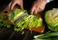 A man hands cut cabbage with a knife on a kitchen cutting board. The idea of shredding cabbage at home