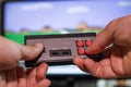 A man`s hands hold an old-fashioned game console controller in front of a TV screen with a game Royalty Free Stock Photo