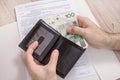 The man`s hands hold a wallet from which they remove PLN banknotes. The tax declaration is in the background on the countertop.