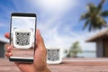 Man`s hands holding smartphone scanning QR code on coffee cup beside the beach