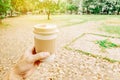 Man`s hands holding take away paper coffee cup with morning hot drink with inspiring view on abstract park background.