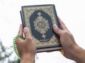 Man`s hands holds Koran - holy book of muslims with Islamic rosary, on blue sky with clouds Royalty Free Stock Photo