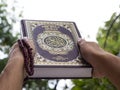 Man`s hands holds Koran - holy book of muslims with Islamic rosary on blue sky with clouds Royalty Free Stock Photo