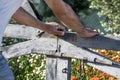 Man`s hands opening or closing Rustic wooden gate of courtyard blooming garden. Summer day floral background Royalty Free Stock Photo