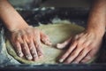 Man`s hands roll out homemade pizza dough by hand, which lies on a dark baking sheet