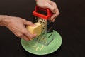 Man`s hands rub cheese on a grater in a green plate