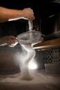 Man's hands sift flour through a metal sieve in a dark kitchen