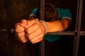 Man's hands tied with rope behind the bars