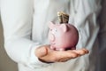 A man`s hands in a white shirt puts a one dollar bills in a pink piggy bank Royalty Free Stock Photo