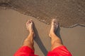 Man`s legs on the sand beach and sea waves at sunset Royalty Free Stock Photo