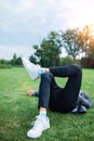 Legs in white sneakers lying on the grass at sunset time. Spring summer vacation relax concept Royalty Free Stock Photo