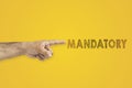 A man`s pointing hand next to the inscription mandatory on yellow background. Royalty Free Stock Photo