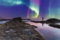 ManÃ¢â¬â¢s reflection silhouette as a Green Aurora borealis shimmers over the ocean water