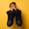 The man`s right hand holding a pair of shoes through the yellow paper background. Royalty Free Stock Photo