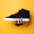 The man`s right hand holding a pair of shoes through the yellow paper background. Royalty Free Stock Photo