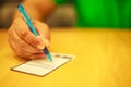 Man`s right hand writing on the lucky draw coupon, memo, comment, suggestion or questionnaires on the wooden table in restaurant