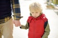 Man with sad little boy are walking hand in hand along city street. Frustrated child does not want to go to kindergarten,