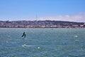 Man sailboarding on choppy bay waters with distant San Francisco shoreline