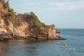 Man sailing in a yellow canoe on the ocean against the rocky cliff covered with trees