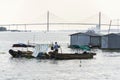 Man sails on ratty boat with fish farm raft houses floating on Mekong river with Rach Mieu Bridge in background Royalty Free Stock Photo