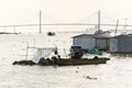 Man sails on ratty boat with fish farm raft houses floating on Mekong river with Rach Mieu Bridge in background