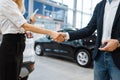 Man and saleswoman shake hands in car dealership