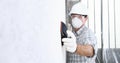 Man sand the wall with sandpaper, professional construction worker with mask, safety hard hat, gloves and protective glasses. Royalty Free Stock Photo