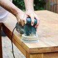 Man sanding an oak table with a random orbital sander.