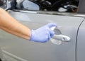 Man sanitizing door handle of his car outdoors. Male hand in protective glove holding sanitizer closeup